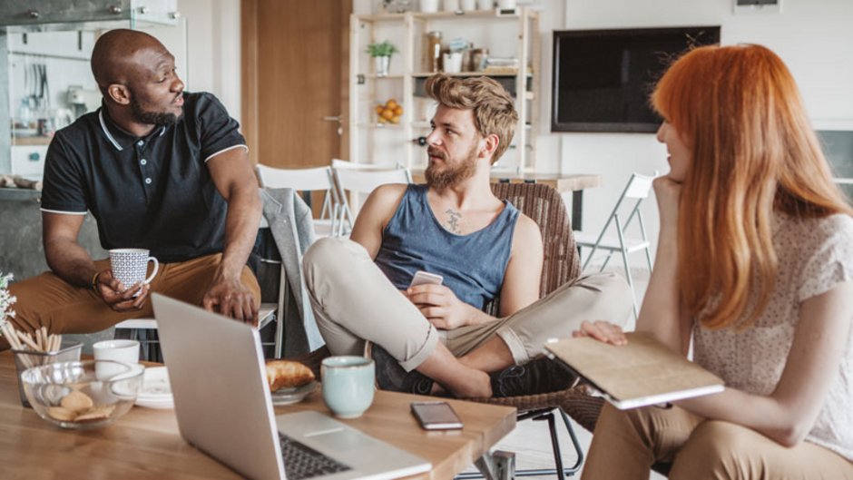 WG-Mietvertrag, Foto von zwei jungen Männern und einer jungen Frau in einem Gemeinschaftsraum beim Unterhalten, Foto: iStock.com / svetikd