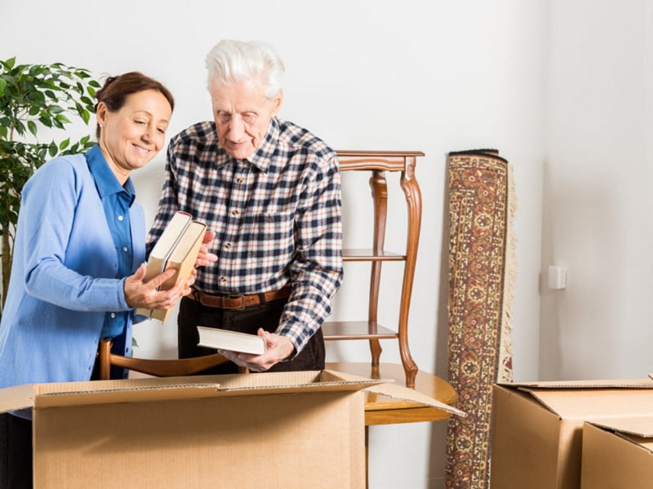 Haushaltsauflösung, Aussortieren, Entrümpeln, Frau packt mit älterem Mann Bücher in einen Karton, Foto: iStock/FredFroese