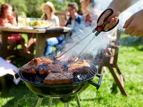 Grillen, Rasenmähen, Nacktsonnen, Mann grillt Steaks und Rauch steigt auf, im Hintergrund sitzen Menschen, Foto: Syda Productions/stock.adobe.com